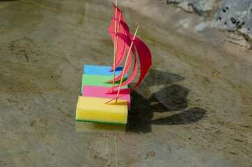 A line of Four children's colorful ships in clear water. Toy sailboats are made from kitchen sponges. Children's sailing regatta in the city fountain. Summer, daytime. Selective focus. No people.