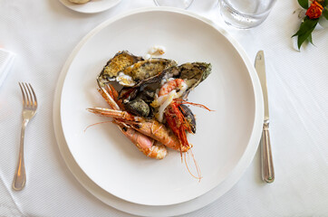 A plate of cooked seafood (prawns, scampi, oysters, mussels, squid) on the white table of a restaurant