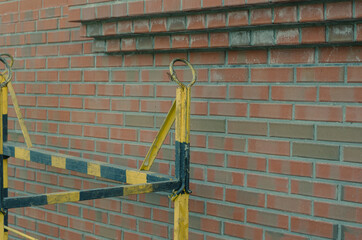Yellow and black construction cradle in front of a red brick building. Metal cradle for lifting people. Round slinging points. Architecture. Selective focus. No people.