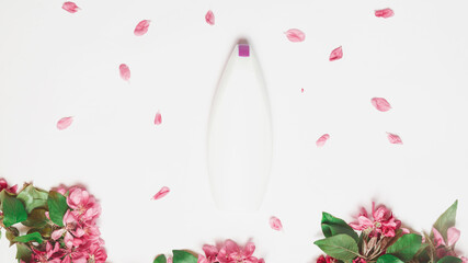 White bottle of natural herbal shampoo for women on white background. Beautiful Fresh branches of apple blossoms. Beauty and care concept. Space for text