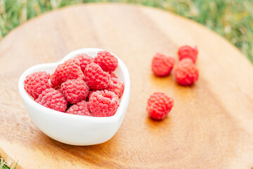 Heart shaped bowl full of ripe red juicy raspberries, on wooden background