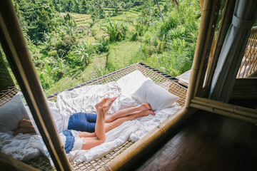 A pair of legs of a man and a woman lie on a hammock in a villa overlooking the rice terraces.