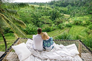 A couple in love sits in a villa in Bali and admires the view of the rice fields.