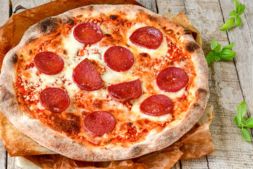 Home made italian  pepperoni   pizza with  tomatoes, mozzarella and parmesan cheese and fresh basil  on wooden background