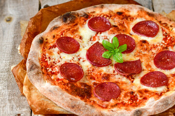 Home made italian  pepperoni   pizza with  tomatoes, mozzarella and parmesan cheese and fresh basil  on wooden background