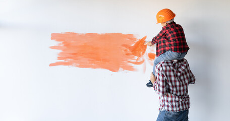 renovating his house, the father is holding his son and helping him paint the wall with a brush. Father's day. Baner.