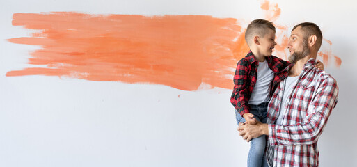 Happy young family is renovating their house. Dad is holding his son in his arms. White wall in the...