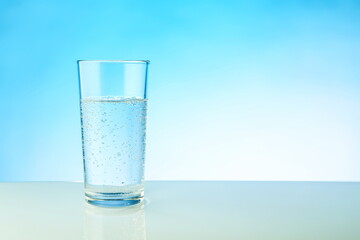 glass of sparkling water on blue background with copy space. mineral water with gas bubbles in a glass on a light blue background