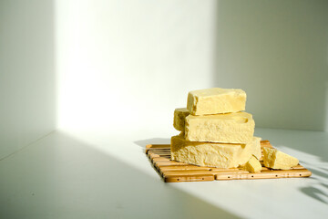 Isolated bars, pieces of cocoa butter on a wooden plate on a white background with shadow. Benefits of cocoa butter for beauty and health. Organic natural products. Minimalism and simplicity. 