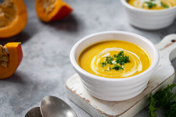 Pumpkin soup with coconut milk and squash slices. Creammy autumn soup in white bowl on gray background.