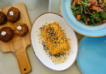 Overhead view at traditional Greek zucchini meatballs, feta cheese fried with crust, honey and sesame seeds and salad. Mediterranean cuisine tavern.