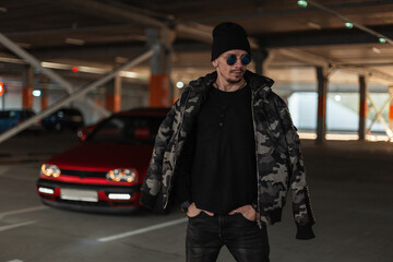 Cool Guy in a Military Jacket with Glasses and Hat Walking Outdoors in a Parking Lot