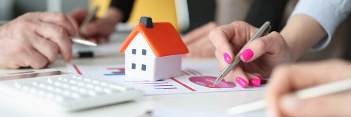 Hands of employees with pens and business charts and small house on table