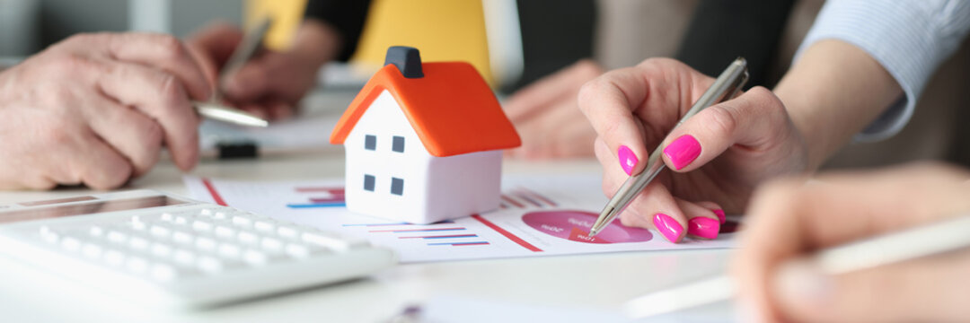 Hands of employees with pens and business charts and small house on table