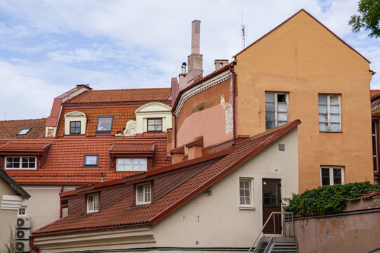 Abstract conceptual architecture of vintage roofs of houses with windows, balconies and oven and ventilation pipes against blue sky with clouds in old Town. Apartments in the attic against skyline