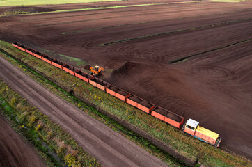 Wheel loader loads peat in freight cars. Aerial view of diesel locomotive on railroad in landscape at wetlands. Drone view of peat bog railway at peatlands. Transporting peat from peat extraction.