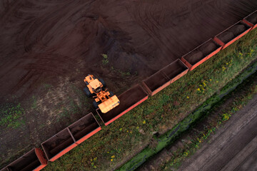 Wheel loader loads peat in freight cars. Aerial view of diesel locomotive on railroad in landscape at wetlands. Drone view of peat bog railway at peatlands. Transporting peat from peat extraction.