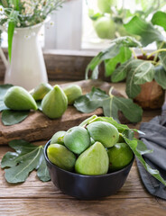 Green figs in grey bawl and wooden table with leaves 