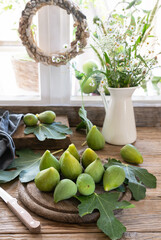 Green figs on the wooden cutting board with leaves and wild flowers