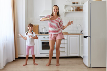 Indoor shot of happy positive family dancing happily together, making the same moving, looking smiling at camera, wearing casual style clothing, childhood and parenthood.