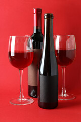 Bottles and glasses of wine on red background