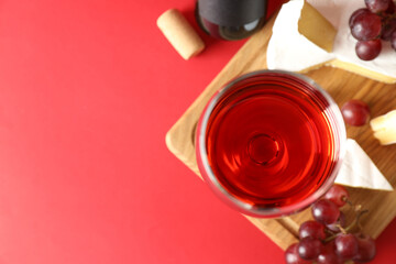 Board with wine, cheese and grape on red background