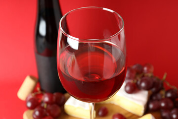 Board with wine, cheese and grape on red background