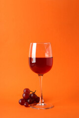 Glasses of red wine and grape on orange background