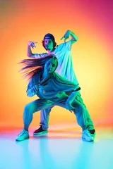Foto auf Leinwand Young hip-hop dancers, stylish emotive girl and boy in action and motion in casual sports youth clothes on gradient multi colored background at dance hall in neon light. © master1305
