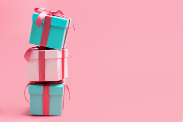 Three gift boxes stand on top of each other close-up on pink background.