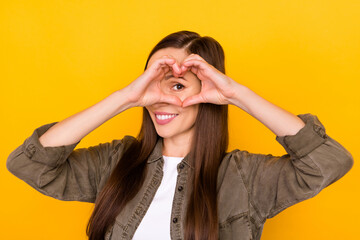 Photo of pretty happy young woman make fingers heart shape look eye smile isolated on yellow color background