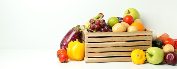 Wooden box with different vegetables and fruits on white table