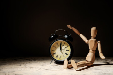 Wooden mannequin with alarm clock on dark background