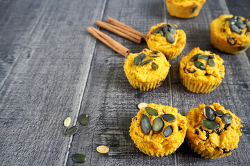 Eight gluten-free pumpkin muffins, sprinkled with pumpkin seeds, lies on a wooden table next to three cinnamon sticks. side view. vegan sweets made at home