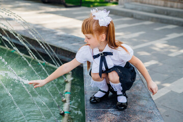 A little girl, an elementary school student, is playing merrily near the fountain .The child will refresh himself on a hot day. - Powered by Adobe