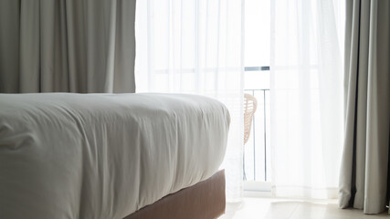 Hotel room with white sheets and curtains and a small terrace. Sunlight enters the room on a sunny...