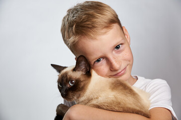 Boy 10 years old tenderly hugs his pet Siamese cat