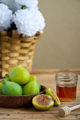 Close-up of wooden bowl with figs, jar of honey and basket with white flowers, selective focus, on wooden table, vertical, with copy space