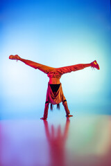 Young sportive girl dancing break dance alone isolated on colorful background at dance hall in neon...
