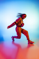Young sportive girl dancing hip-hop in stylish clothes on colorful background at dance hall in neon...