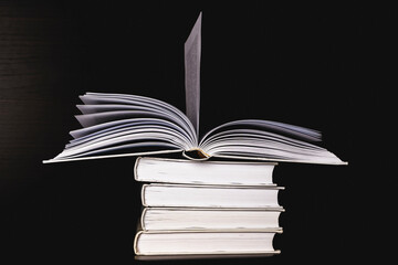 A stack of white blank books on a shelf on a black background, free space for copying, without labels, an empty spine.