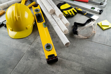 Fototapeta premium Contractor concept. Tool kit of the contractor: yellow hardhat, libella, hand saw. Plans and notebook on the gray tiles background.