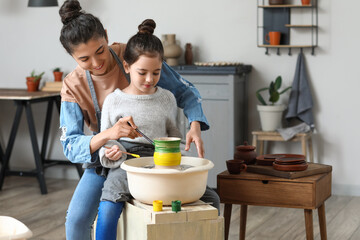 Little girl with her mother painting ceramic pot at home