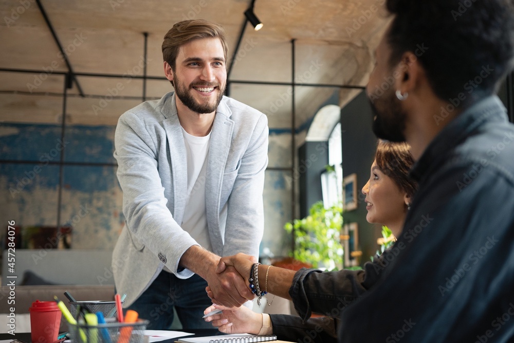 Canvas Prints Two men shaking hands and looking at each other with smile while their coworkers sitting at the business meeting