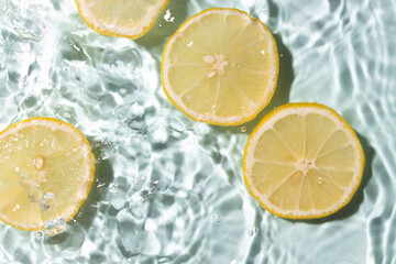 Bright cosmetics background.Top view and closeup of slices of fresh lemon in the water.Vitamin ingredients
