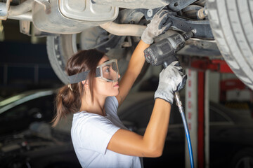 A young woman fixing the underbody of a car with a  impact wrench in a garage.
