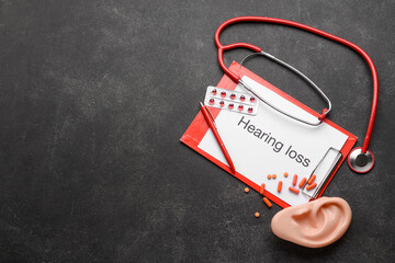 Clipboard with text HEARING LOSS, stethoscope and ear model on dark background