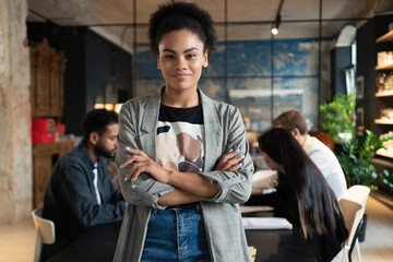 Successful smiling mixed-race businesswoman standing in creative office and looking at camera at modern office