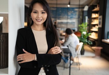 Successful smiling asian businesswoman standing in creative office and looking at camera at modern office