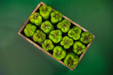 Green bel peppers or capsicum in a wooden basket on a plain background with selective focus and blur